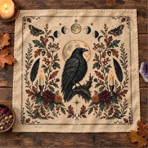 May include: A square beige fabric cloth featuring a central black raven perched on a branch against a full moon. The design includes lunar phases, two lit candles in holders, feathers, moths, oak leaves, acorns, and flowers in a symmetrical layout.