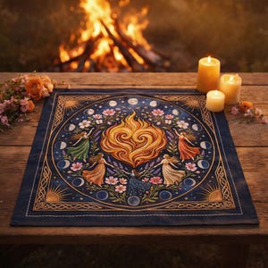 K&ouml;nnte beinhalten: Ein dunkelblaues quadratisches Wandtuch mit einem zentralen Flammendesign, umgeben von Figuren, Blumen und Mondphasen. Das Wandtuch hat einen goldenen Rand und liegt auf einem Holztisch mit Kerzen und Blumen.