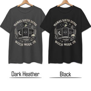 K&ouml;nnte beinhalten: Zwei T-Shirts, eines dunkelgrau und eines schwarz, werden gezeigt. Jedes Shirt hat eine kreisf&ouml;rmige Grafik mit dem Text "MAMA'S SIXTH SENSE" und "WITCH MODE ON". Die Grafik enth&auml;lt Tarotkarten, einen Totenkopf und Himmelselemente.