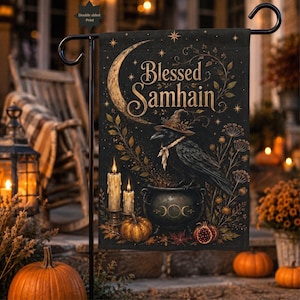 Puede incluir: Una bandera de jardín negra con el texto Blessed Samhain, una luna creciente, un cuervo con sombrero de bruja, un caldero con un símbolo de triple luna, dos velas encendidas, una calabaza, una granada e ilustraciones botánicas de hojas y estrellas.