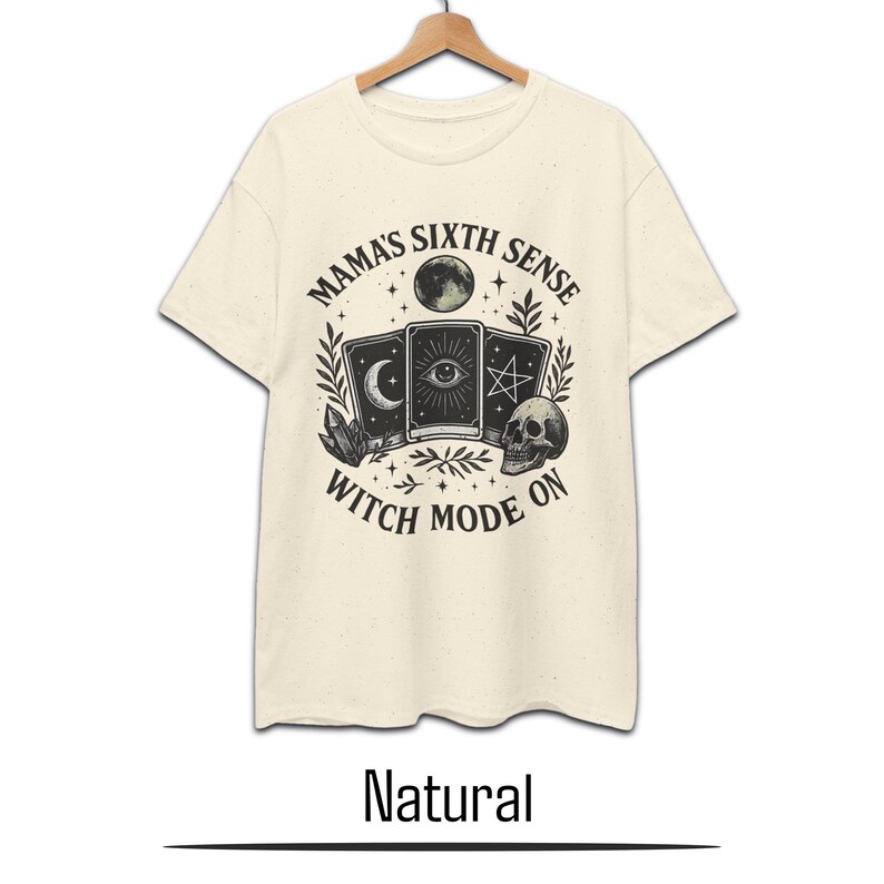 K&ouml;nnte beinhalten: Cremefarbenes T-Shirt mit einem Grafikdesign mit Tarotkarten, einem Totenkopf und dem Text "Mama's Sixth Sense Witch Mode On". Das Design beinhaltet einen Mond, ein Auge und Sterne. Das Wort "Natural" ist unten aufgedruckt.