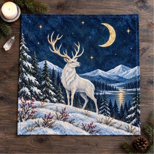 Puede incluir: Un tapiz cuadrado de tela que muestra un ciervo blanco de pie en un paisaje nevado por la noche. La escena incluye un cielo estrellado azul oscuro, una luna creciente, pinos cubiertos de nieve, montañas lejanas y un lago reflectante.