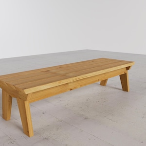 Puede incluir: Un banco de madera de color claro con una parte superior rectangular y patas anguladas. El banco está hecho de madera natural y tiene un diseño simple y minimalista. El banco mide aproximadamente 152 cm de largo.