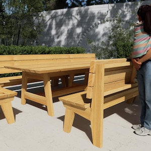 May include: A light-coloured wooden outdoor dining set consisting of a rectangular table, two long benches with backrests, and a single chair. The furniture features a natural wood grain finish, sturdy angled legs, and horizontal slat backrests.