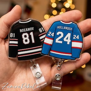 May include: Two hockey jersey-shaped badge reels. One is black with white and red stripes, the name "ROZANOV" and the number "81". The other is blue with red and white stripes, the name "HOLLANDER" and the number "24".