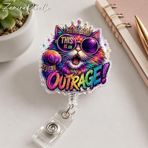 May include: A clear acrylic badge reel featuring a colourful, illustrated cat wearing a jewelled crown and round sunglasses. The cat has an open mouth and is surrounded by small star accents. The text reads THIS IS AN OUTRAGE! in bold letters.