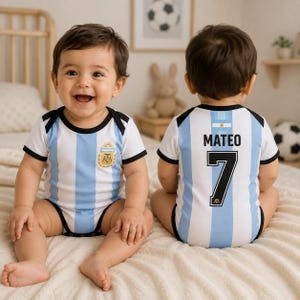 Puede incluir: Un body para bebé con las rayas verticales azul claro y blancas de la selección nacional de fútbol de Argentina. El frente muestra el escudo de la AFA, mientras que la espalda presenta el nombre MATEO sobre el número 7 en negro y un emblema.