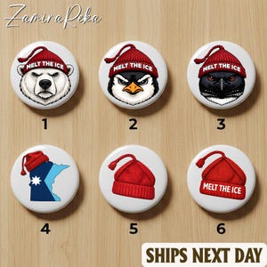 May include: A collection of six white round buttons. The buttons feature illustrations of a polar bear, penguin, and raven wearing red knit caps with the text "MELT THE ICE". Other buttons show a red knit cap and a map. The buttons are on a wooden surface.