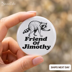Op de afbeelding: Een ronde witte button met een zwart-witte illustratie van een lopende wasbeer. De tekst "Friend Of Jimothy" is in een vetgedrukt zwart schreeflettertype onder de wasbeerafbeelding op het oppervlak van de ronde button gedrukt.