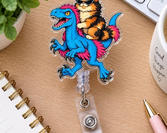Puede incluir: Un portatarjetas de acrílico transparente con una ilustración colorida de un dinosaurio azul con plumas rosas que lleva un gato calicó esponjoso con una corona rosa y gafas de sol negras. Incluye un cordón retráctil y un clip de metal.