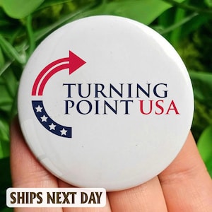 Puede incluir: Botón blanco con el texto "TURNING POINT USA" en azul marino y rojo. El botón presenta una flecha roja y un arco azul marino con estrellas blancas. Las palabras "SHIPS NEXT DAY" están en la parte inferior.