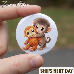 May include: A round white button featuring two cartoon monkeys hugging. One monkey is brown, and the other is orange. The button has the text "SHIPS NEXT DAY" at the bottom.
