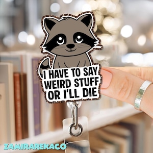 May include: A retractable badge reel featuring a cartoon raccoon with a black mask and a glittery border. The text "I HAVE TO SAY WEIRD STUFF OR I'LL DIE" is displayed on the badge. The reel has a clear plastic strap and a metal clip.
