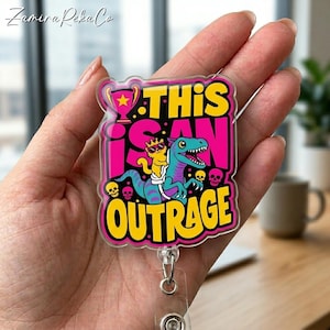 May include: A clear badge reel with a colorful design featuring a cartoon dinosaur and a yellow creature wearing sunglasses, with the text "THIS IS AN OUTRAGE". The badge reel has a clear plastic strap and a metal clip.