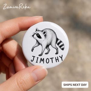 Op de afbeelding: Een ronde witte button met een zwart-witte inktillustratie van een lopende wasbeer. Onder de wasbeer staat de naam JIMOTHY in dikke, zwarte, schreefloze hoofdletters gedrukt op het witte oppervlak van de button.