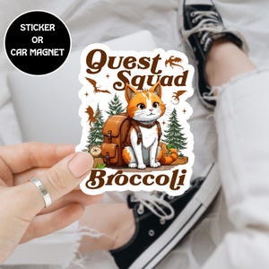 May include: A sticker or car magnet featuring a cartoon cat with orange and white fur, wearing a backpack. The text "Quest Squad Broccoli" is above and below the cat, with dragon and tree illustrations.