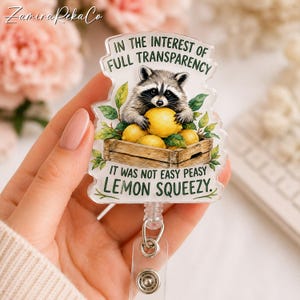 Könnte beinhalten: Ein transparenter Ausweishalter aus Acryl mit einem Waschbären, der gelbe Zitronen in einer Holzkiste hält. Der Text lautet: IN THE INTEREST OF FULL TRANSPARENCY IT WAS NOT EASY PEASY LEMON SQUEEZY. Das Design enthält grüne Blätter und einen Metallclip.