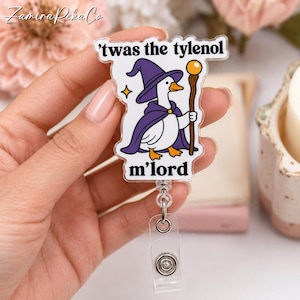May include: A clear acrylic badge reel featuring a cartoon white duck dressed as a wizard in a purple hat and cape, holding a wooden staff with a yellow orb. The text 'twas the tylenol m'lord' is printed in black above and below the duck illustration.