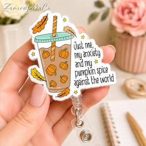 Könnte beinhalten: Ein transparenter Ausweishalter aus Acryl mit einer Grafik eines Eiskaffeebechers, gefüllt mit brauner Flüssigkeit und kleinen orangefarbenen Kürbissen. Der Text lautet, Just me, my anxiety and my pumpkin spice against the world, mit gelben Sternen.