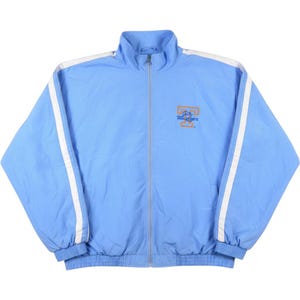 May include: A light blue zip-up jacket featuring a high collar, long sleeves with white vertical stripes, and ribbed cuffs and hem. The front displays an orange letter T logo with the text Volunteers embroidered in blue on the left chest area.