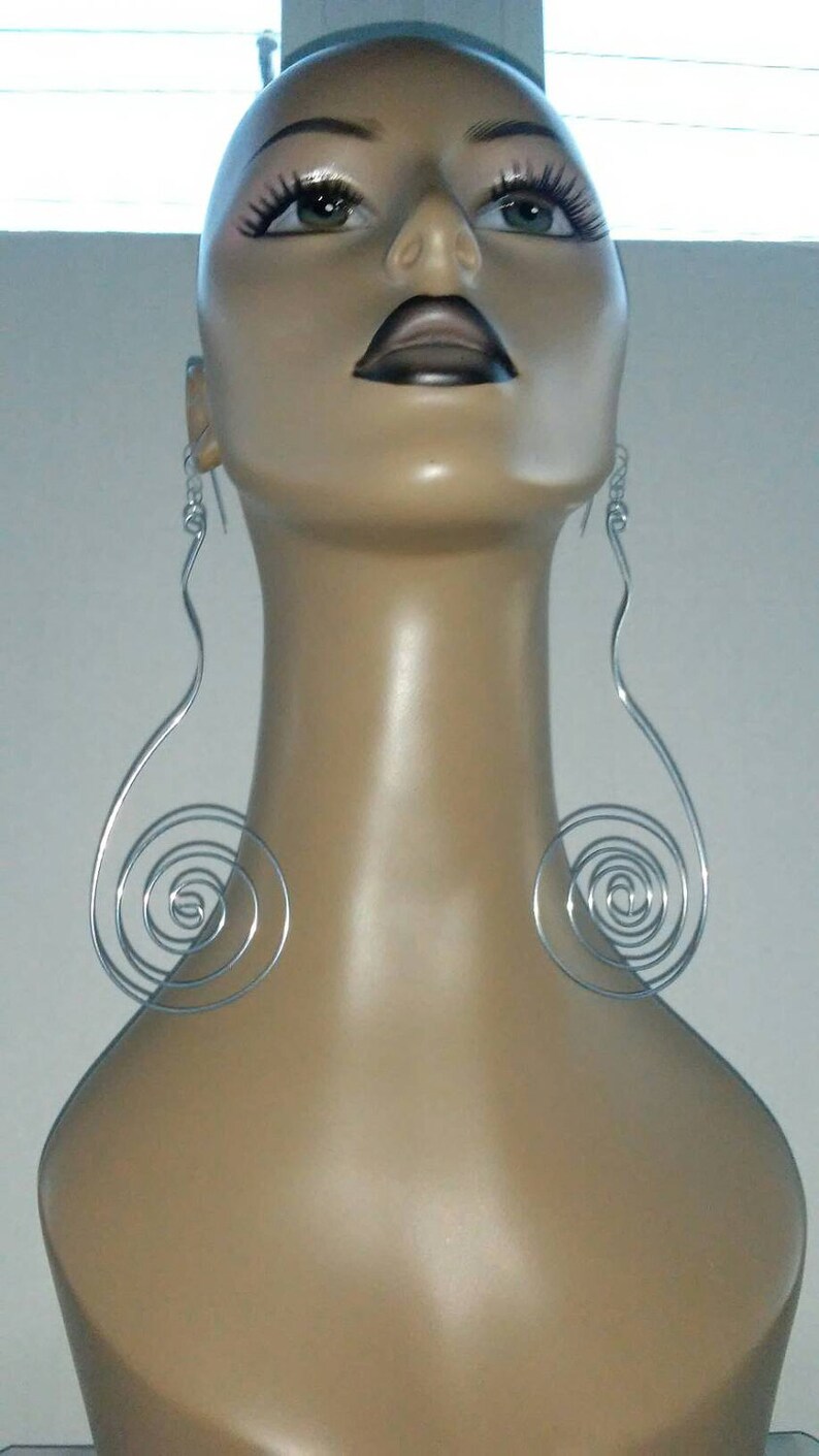 Op de afbeelding: Een mannequin met een paar zilveren spiraalvormige oorbellen. De oorbellen zijn lang en hangen van de oorlelletjes. De mannequin heeft een neutrale uitdrukking en kijkt recht vooruit.