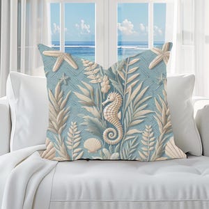 Peut inclure: Un coussin carré avec un fond bleu clair présentant un motif texturé de hippocampes, d'étoiles de mer, de coquillages et de diverses plantes aquatiques de couleur crème. Le motif est répété sur toute la surface de la housse de coussin.