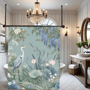 Puede incluir: Una cortina de ducha con un diseño botánico que presenta una garza, flores de loto y glicinias en tonos azules, verdes y blancos. La cortina está en un baño con una lámpara de araña y un tocador de madera.