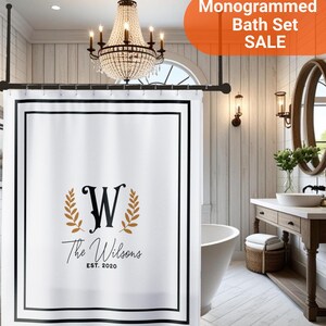 May include: A white shower curtain featuring a black rectangular border, a central black letter W flanked by two gold laurel branches, and the text The Wilsons EST. 2020. The curtain hangs from a black rod with metal rings in a bathroom setting.