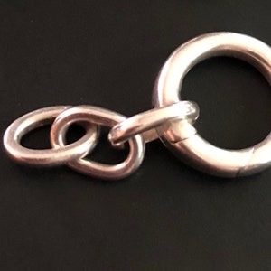 May include: Silver chain with a large, round, silver clasp. The clasp is open and ready to be attached to a necklace or bracelet.