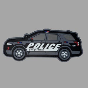 May include: A black and grey patch depicting a police SUV. The word 'POLICE' is in large white letters on the side, with 'ALPHA KILO DESIGNS' below. The number '911' is also visible.