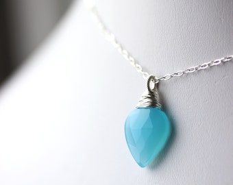May include: A silver chain necklace with a light blue gemstone pendant. The pendant is wrapped in silver wire and has a faceted, heart-shaped design.