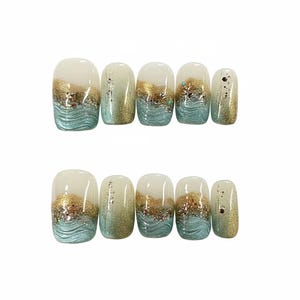 Peut inclure: Un ensemble de dix faux ongles avec un motif comprenant une base transparente, des paillettes dorées et un motif de vagues turquoise. Les ongles sont de formes variées, ovales et rectangulaires.