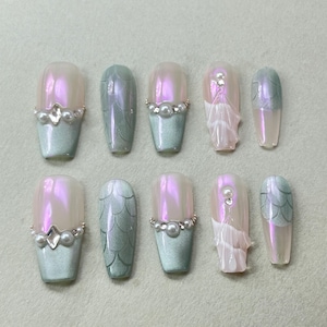 Puede incluir: Un conjunto de diez uñas postizas con acabado nacarado. Las uñas presentan un degradado de color, pasando del rosa claro al verde mar. Algunas uñas están adornadas con perlas y pedrería, mientras que otras tienen un diseño texturizado.