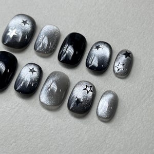 Könnte beinhalten: Satz mit zehn kurzen, silbernen und schwarzen falschen Nägeln mit Sternenmuster. Die Nägel sind ombre mit einem Farbverlauf von Silber zu Schwarz.