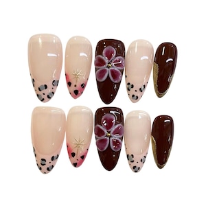 Puede incluir: Un conjunto de diez uñas artificiales con varios diseños. Algunas uñas son nude con puntas con estampado de leopardo negro y gris. Otras presentan una base burdeos con un diseño floral en 3D. Una uña tiene un acento de purpurina dorada.