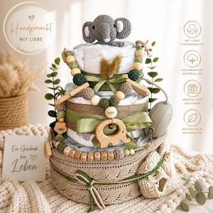 Könnte beinhalten: Eine Windeltorte mit einem gehäkelten grauen Elefanten, verziert mit grünen Bändern, Holzperlen und einem Holzelefanten. Die Basis ist ein gestrickter Korb mit Babyschuhen. Die Karte sagt "Ein Geschenk fürs Leben".