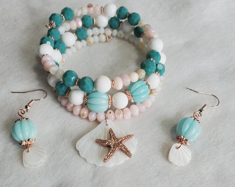 May include: A multi-strand bracelet with white, pink and teal beads, accented with a seashell charm and a starfish. Matching earrings with teal beads and seashell charms.