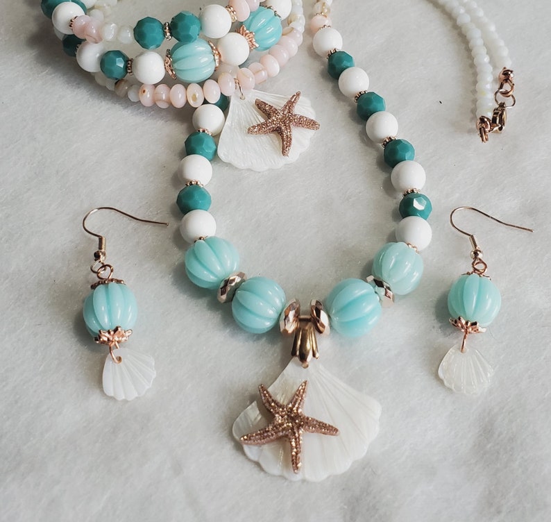 May include: A white and turquoise beaded necklace with a seashell pendant and starfish charm. The necklace is paired with matching earrings featuring seashells.