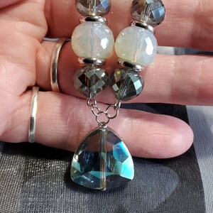 May include: A silver chain necklace with alternating clear, iridescent, and dark gray beads. The necklace has a large, teardrop-shaped, iridescent crystal pendant.