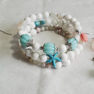 May include: A set of white and blue beaded jewellery with starfish and seashell charms. The bracelet is made of white beads with blue and pink accents. The earrings are made of white beads with blue and pink accents and a starfish charm.