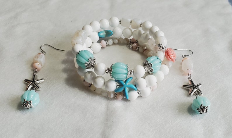May include: A set of white and blue beaded jewellery with starfish and seashell charms. The bracelet is made of white beads with blue and pink accents. The earrings are made of white beads with blue and pink accents and a starfish charm.