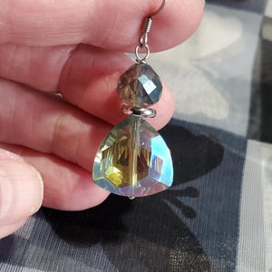May include: A pair of iridescent crystal earrings with a teardrop-shaped crystal and a smaller round crystal. The earrings are silver-toned and have a hook closure.