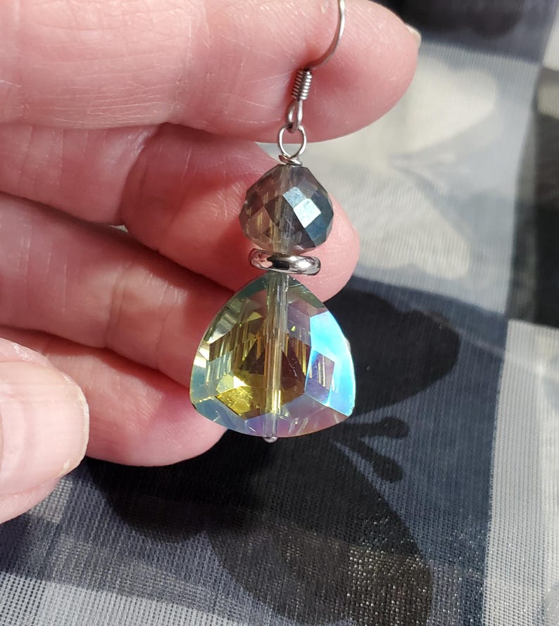 May include: A pair of iridescent crystal earrings with a teardrop-shaped crystal and a smaller round crystal. The earrings are silver-toned and have a hook closure.