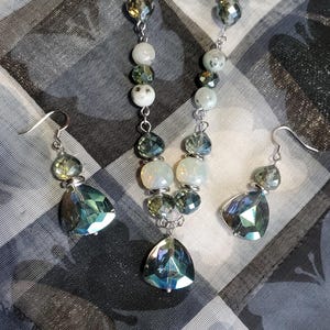 May include: A silver necklace and earrings set with iridescent green and white beads. The necklace features a teardrop-shaped pendant.