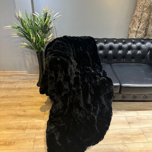 May include: A black faux fur throw blanket draped over a black leather sofa. The blanket has a soft, plush texture and is perfect for adding warmth and style to any room.
