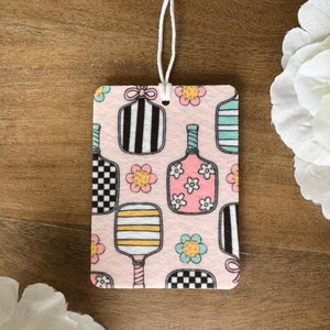 May include: A pink car air freshener with a pattern of colorful paddleball rackets and flowers.