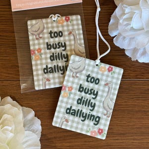 May include: Two rectangular air fresheners with a gingham pattern, geese illustrations, and the text "too busy dilly dallying." The air fresheners have a white string for hanging and are decorated with floral accents.