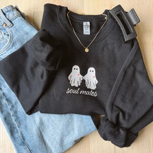 May include: Black sweatshirt with a white embroidered design of two ghosts holding hands with a red heart. The text "soul mates" is embroidered below the ghosts.