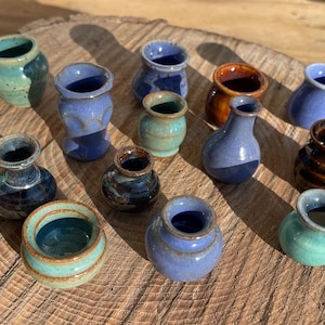 Puede incluir: Una colección de quince jarrones de cerámica en miniatura de diversas formas y tamaños, con una paleta de colores variada que incluye tonos azules, verdes, marrones y rosas, con acabados esmaltados brillantes y cuellos definidos.