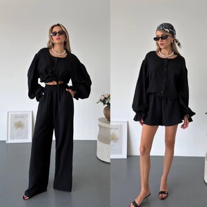 May include: A black two-piece set consisting of a long-sleeved button-down top with voluminous sleeves and matching bottoms. The left side shows wide-leg trousers, while the right side shows shorts. Both outfits feature a textured fabric and pearl necklace.